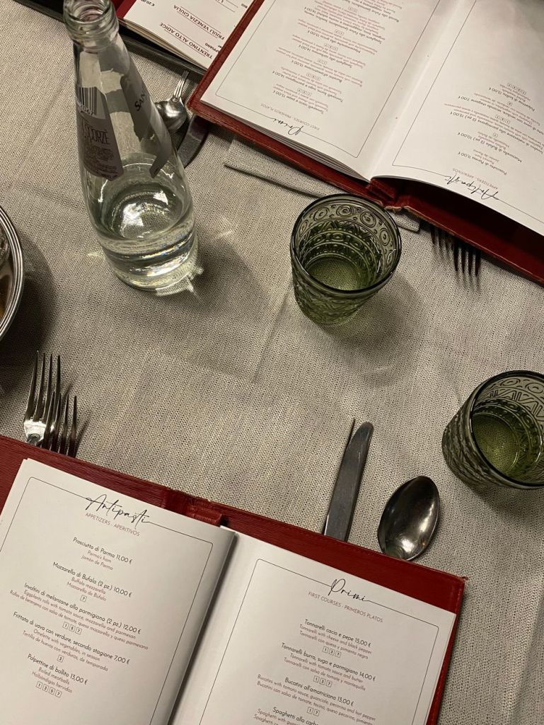 open menu glasses bottle of water and cutlery on gray tablecloth